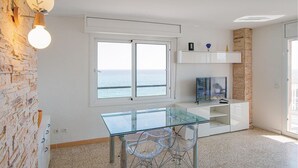 Una stanza con tavolo e sedie in vetro, televisione, finestra vista mare e parete in mattoni.