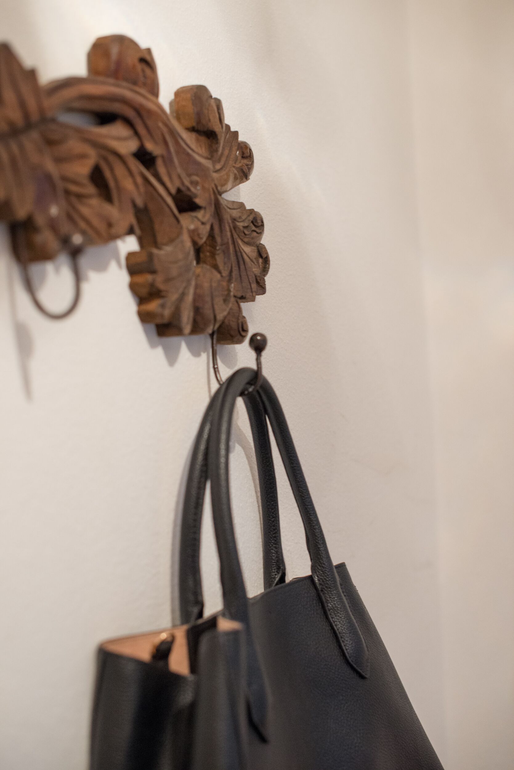 A black leather handbag hanging on a wall-mounted hook.