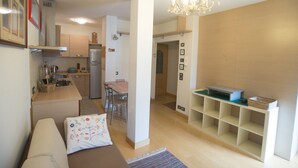 Un espacio habitable compacto con kitchenette, comedor y zona de estar con sofá y una mesita.