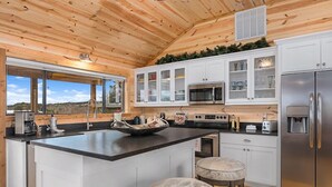 A modern kitchen with a large island, white cabinetry, stainless steel appliances, and a view of the outdoors. - No Rancho Properties Texas Haus | Hot Tub | Beautiful Views (Fredericksburg)