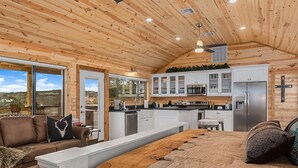 A log cabin interior with a central island, a sofa, and a bed. - No Rancho Properties Texas Haus | Hot Tub | Beautiful Views (Fredericksburg)