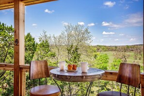 Eine Holzterrasse mit einem runden Tisch und zwei Stühlen, mit Blick auf eine schöne Landschaft aus Bäumen und Hügeln.
