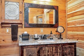 Ein Badezimmer einer Holzhütte mit einer Granit-Arbeitsplatte, einem Spiegel, einem Handtuchhalter und einem Holzkabinett.