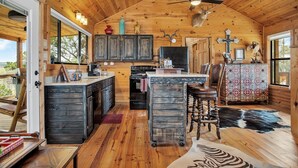 L’intérieur d’un chalet rustique, avec des murs en bois, un îlot central doté de tabourets de bar, un ventilateur de plafond et une grande fenêtre.