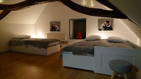 A cozy attic bedroom with two beds, wooden floors, and a sloped ceiling.