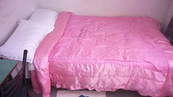 A small, single-bed room with a pink bedspread, a white pillow, and a blue item on the floor.