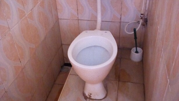 A small, tiled bathroom with a toilet, a bidet, and a toilet paper holder. - Perma Hotel (Wote)