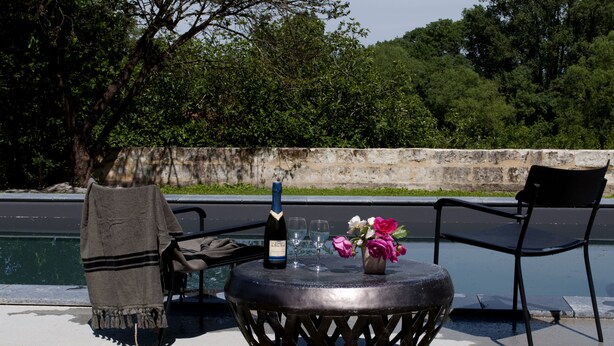 A round table with a bottle and glasses, a chair, and a blanket by a poolside. - Cottage overlooking Loire (Chênehutte-Trèves-Cunault)
