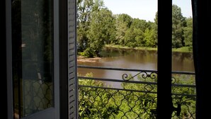 A room with a view of a river and greenery through a window with a metal railing. - Cottage overlooking Loire (Chênehutte-Trèves-Cunault)
