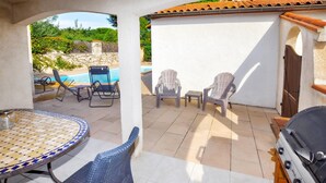 Patio esterno con tavolo e sedie piastrellati, un barbecue e vista su una piscina.