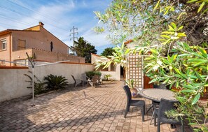 Relax in a serene patio surrounded by lush greenery and a brick wall, featuring a round metal table and four wicker chairs.