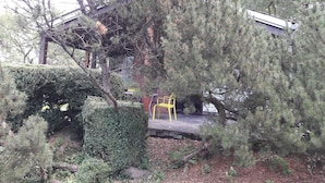 Un espace jardin agrémenté d’une pergola en bois, d’une chaise jaune et d’un petit pont enjambant un sentier de pierres.