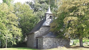 Une petite église en pierre, dotée d’un clocher, entourée d’arbres et bordée d’une pelouse.