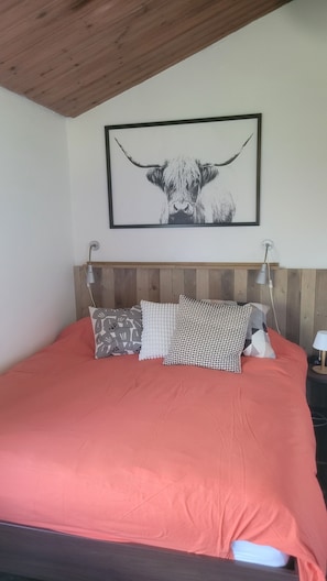 Un lit avec une couvre-lit rouge, une tête de lit en bois et un tableau encadré représentant un taureau accroché au mur.
