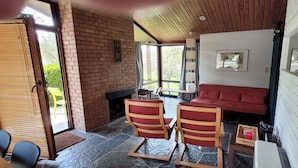 Une pièce chaleureuse avec une cheminée en briques, un canapé rouge et deux fauteuils en bois.