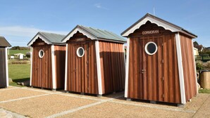 Three wooden portable toilets with white trim and a peaked roof, labeled "PETREL," "GREBE," and "CORMORAN."