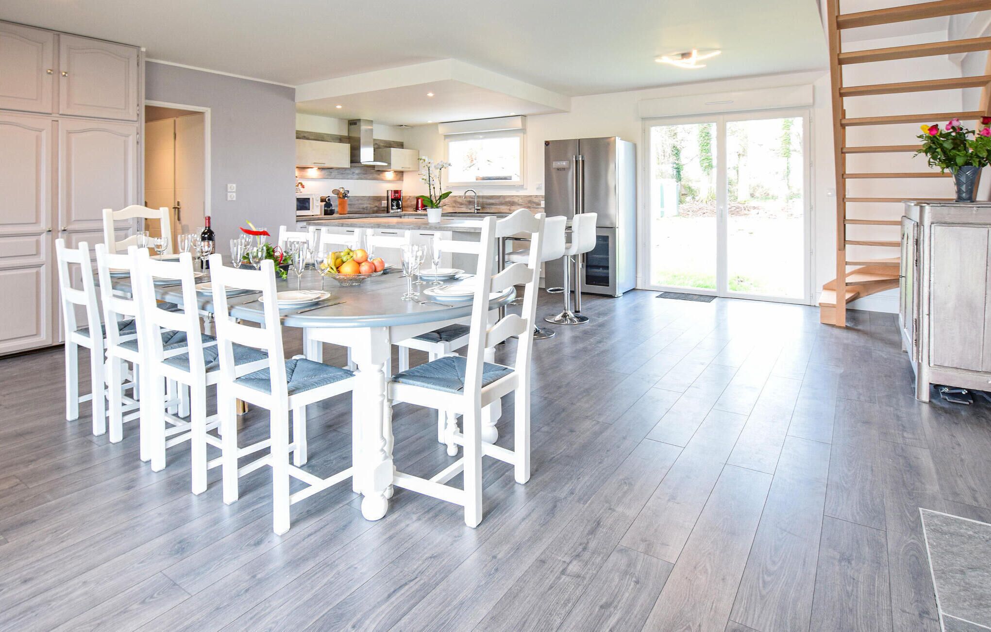 A modern kitchen with white cabinetry, a dining table set for six, and a large window providing natural light.