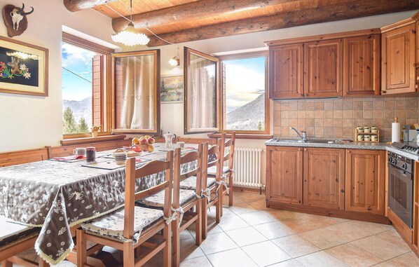 A rustic kitchen with wooden cabinets, a dining table with chairs, and large windows offering a mountain view.
