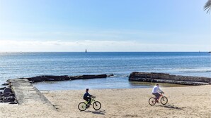 A beach with two cyclists, a clear sky, and the ocean in the background.