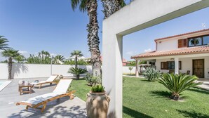 A patio with two lounge chairs, a large vase, and a well-maintained lawn.