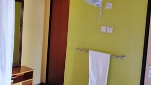 Una habitación con cama, mesita de noche, espejo, ventilador, toallero y puerta.