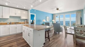 A modern kitchen with white cabinets, a large island, and a dining area with a view of the ocean. - Penthouse Ocean View at Laketown Wharf 1911 (Panama City Beach)