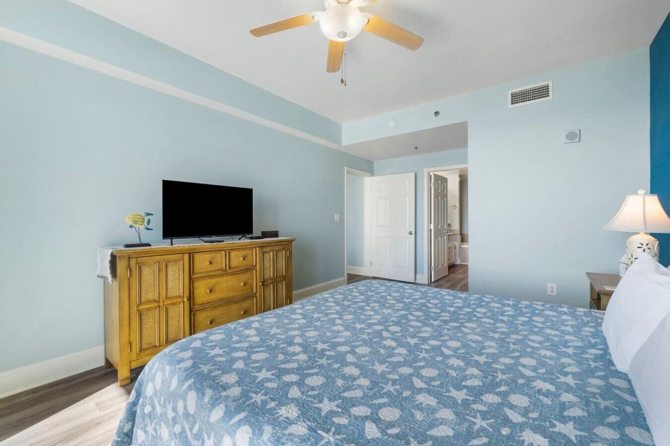 Un dormitorio con cama, cómoda, televisor y ventilador de techo.