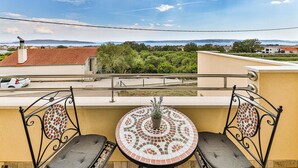 Un balcon avec une table ronde et deux chaises, donnant sur un quartier résidentiel avec des maisons et des arbres.