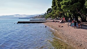 Une plage avec des galets, des arbres et des gens.