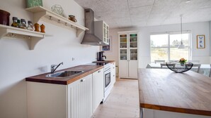 Uma cozinha moderna com armários brancos, bancada de madeira e forno embutido. Há uma janela que oferece iluminação natural e vista para o exterior.