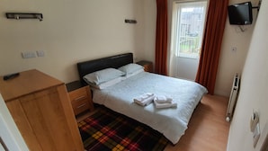 A bedroom with a bed, a wooden nightstand, a TV mounted on the wall, and a door with curtains. - Lovely, Light and Airy 1-bed Flat in Stornoway (Stornoway)