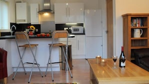 A compact kitchen with white cabinets, a microwave, and a gas stove. There are two foldable chairs and a small table with a candle and wine glasses. - Lovely, Light and Airy 1-bed Flat in Stornoway (Stornoway)