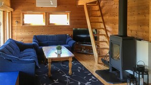 L’intérieur d’un chalet accueillant, avec un canapé, une petite table ornée d’une plante, un téléviseur, une cheminée et une échelle.