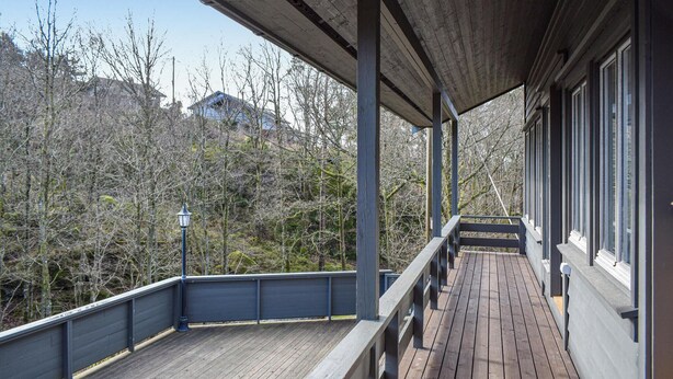 Une terrasse en bois avec une rambarde, un lampadaire et une vue sur des arbres et un bâtiment en arrière-plan.