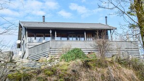 Une cabane en bois dotée d’un balcon, entourée de verdure et de rochers.