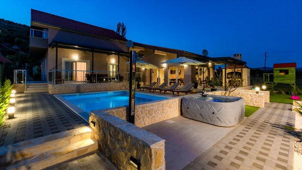 Une maison moderne dotée d’une piscine, d’un espace salon extérieur et d’une terrasse en pierre.