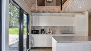 Et moderne køkken med hvide skabe, en marmor bordplade og udsigt til det frie gennem en glasdør.