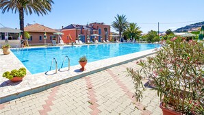 A swimming pool with lounge chairs and umbrellas, surrounded by potted plants and a building with a red facade. - Amazing apartment in Pietra Ligure with WiFi (Pietra Ligure)