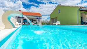 A swimming pool with a water feature, lounge chairs, and a building with a red-tiled roof. - Stunning home in Benkovac (Benkovac)