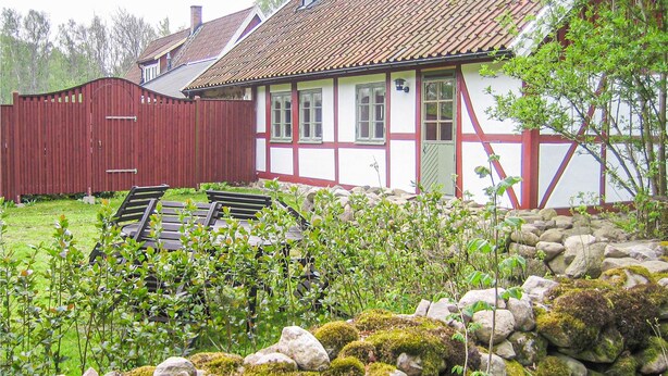 Een traditioneel vakwerkhuis met een rode houten omheining, een stenen muur en een tuin met bankjes.