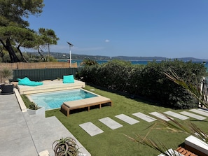 Un jardin avec une piscine, un espace de détente et une vue sur la mer.