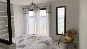 A bedroom with a bed, a chair, a window with a view of the sea, and a ceiling light. - Villa Récampado - Feet in the water, pool and sea (Cavalaire-sur-Mer)