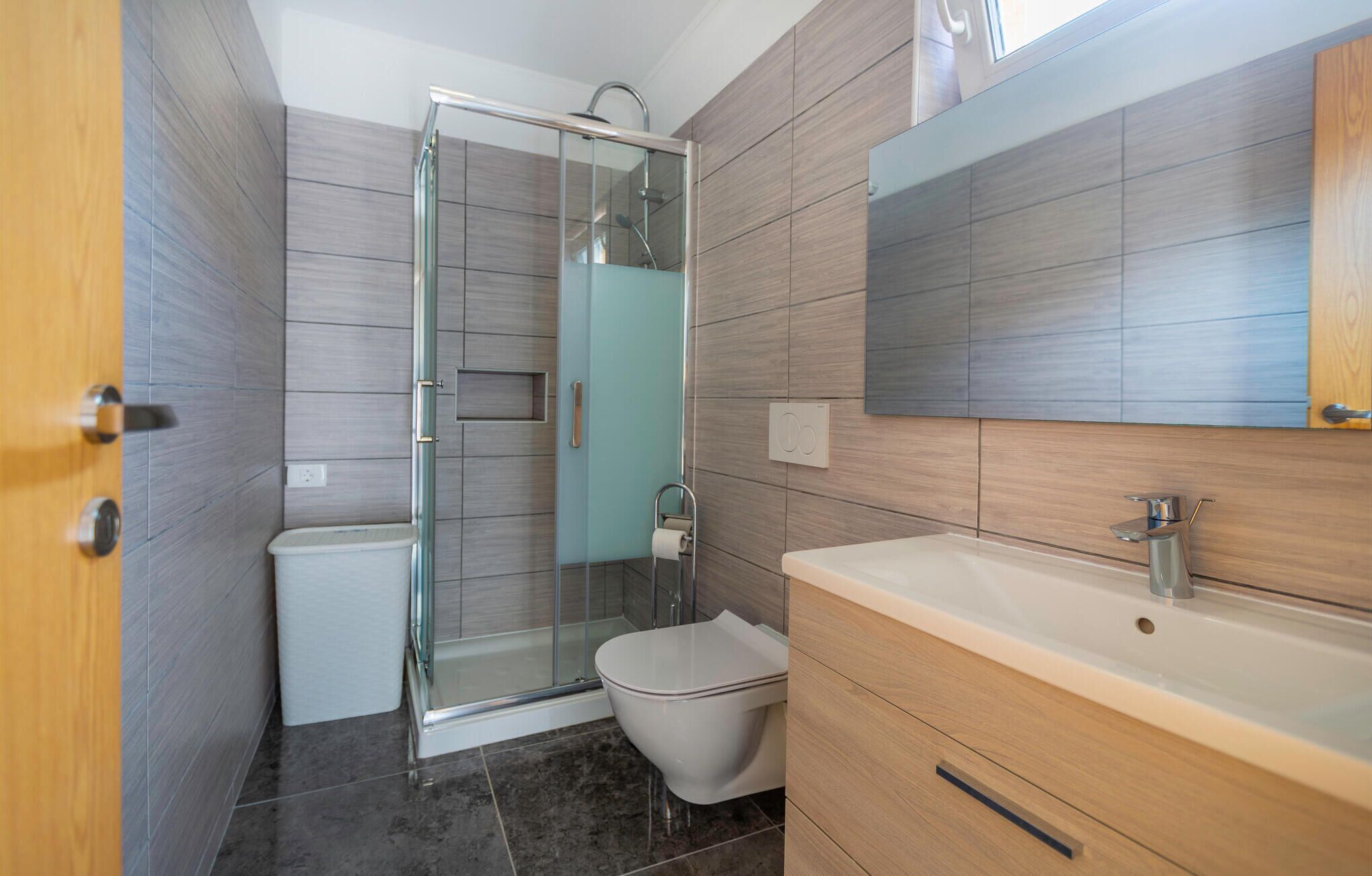 A modern bathroom with a glass shower enclosure, a toilet, a sink with a mirror, and wooden cabinetry.