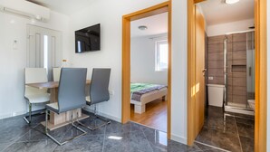 Ein modernes Zimmer mit Schreibtisch, Stühlen, einem Bett und einem Duschbereich.
