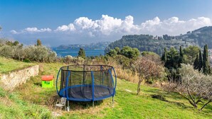 Ein Trampolin auf einer Rasenfläche mit Blick auf eine Küstenlandschaft und entfernte Gebäude.