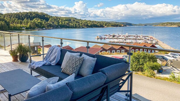 A balcony with a sofa and table overlooking a marina with boats and a lake. - Cozy apartment in Svanesund with WiFi (Svanesund)