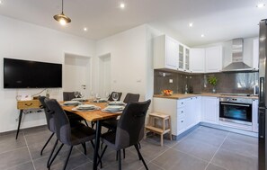 A modern kitchen with white cabinets, a built-in oven, and a dining area with a wooden table and chairs. - Amazing home in Lovrec (Lovrec)