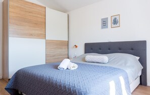 A bedroom with a grey upholstered headboard, a blue quilted bedspread, and a white pillow. There are two framed pictures on the wall, one with text and another with a leaf design. - Amazing home in Lovrec (Lovrec)