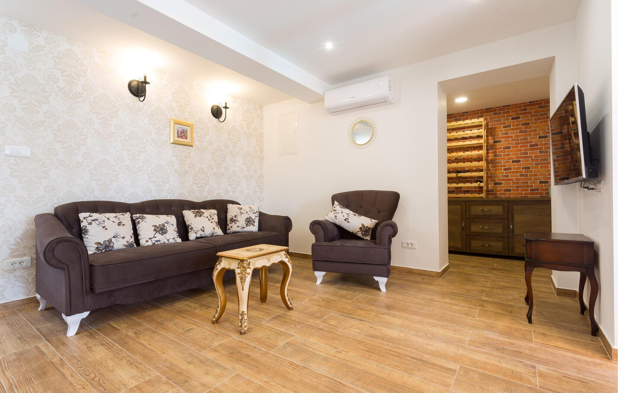 A living room with a brown sofa, a matching armchair, a small wooden coffee table, and a brick wall in the background.