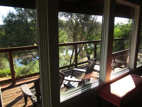 A wooden deck with a bench and a table, overlooking a lake surrounded by trees. - Gorgeous Riverfront Home, VHR# 073569, TOT# T65183 (Lotus)